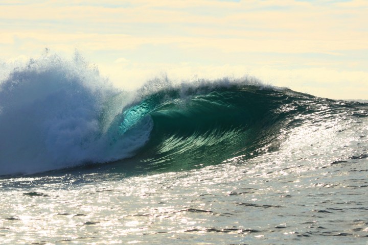 a man riding a wave on a surfboard in the ocean with The Wedge in the background