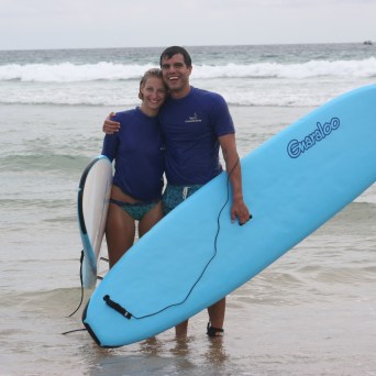 a man standing on a beach holding a surf board