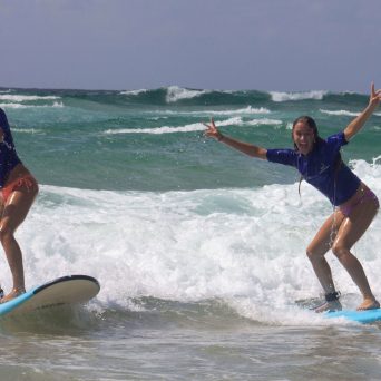 two girls riding a wave on a surfboard in the ocean